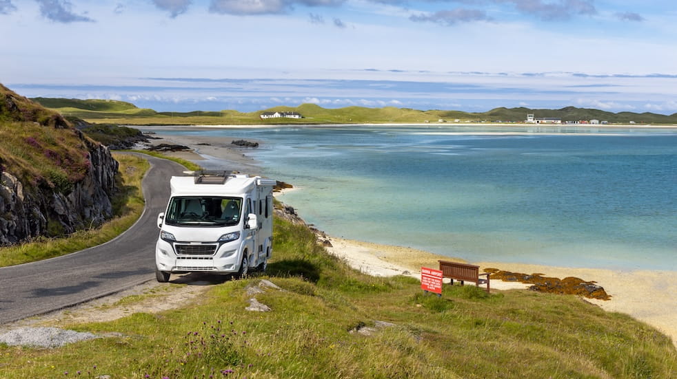 Front view of a motorhome/campervan parked alongside the road with a spectacular view of the ocean and the distant view of Barra Airport in background